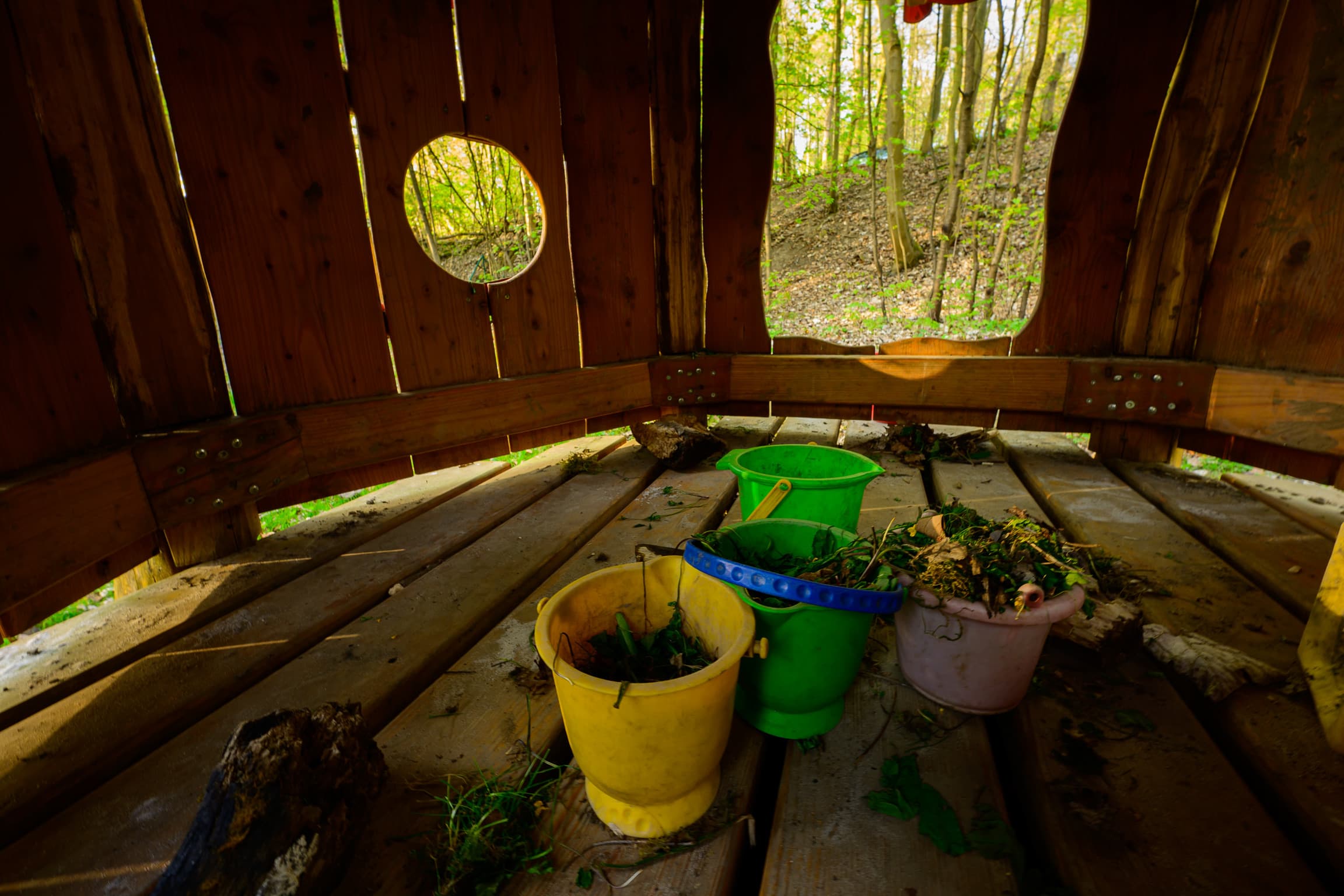Blick aus dem Holzspielhaus auf den Wald – Eimer mit Naturmaterialien